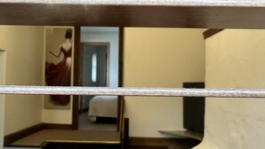 Ein Hotelzimmer mit einem spiegelnden, holzrahmenartigen Spiegel, der ein Bett, einen Nachttisch und eine Wandleuchte zeigt.