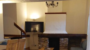 Ein gemütliches Wohnzimmer mit Kamin aus Stein, Holzmöbeln und einem flachbildfernseher an der Wand.
