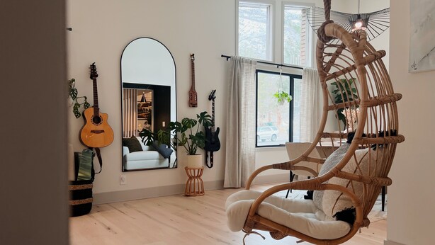Une pièce avec un fauteuil suspendu, une guitare, un miroir et une fenêtre avec des rideaux.