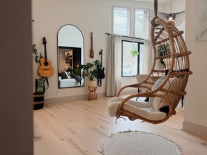 Ein Zimmer mit Hängekorbsessel, Gitarre, Spiegel und einem Vorhangfenster.