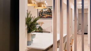 Une cuisine moderne avec des luminaires suspendus, un coin repas avec un banc et une vue sur un couloir.