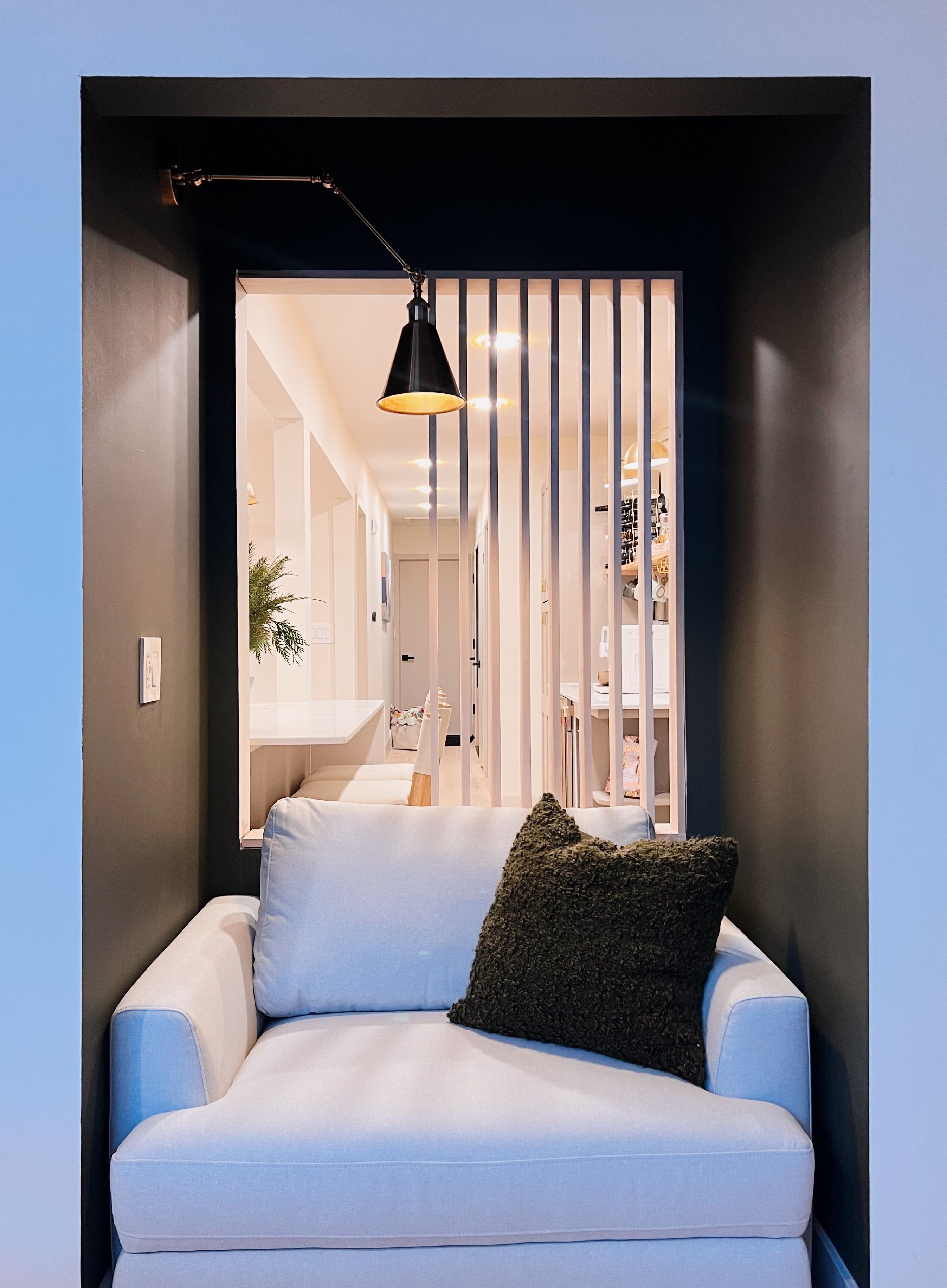 Ein modernes Wohnzimmer mit einem weißen Sofa, einem dunklen strukturierten Kissen und einer schwarzen Pendelleuchte.
