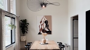 Un espace de salle à manger moderne avec une table en bois, des chaises noires, un luminaire au plafond original et un grand tableau abstrait.