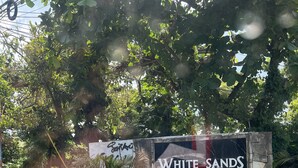 Een bord voor 'White Sands Villas' met een stenen omlijsting en wat groen ervoor.