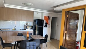 Een moderne keuken met een magnetron, fornuis en koelkast. Er is een eettafel met stoelen en een vaas. De kamer heeft houten vloeren en een geel accentmuur.