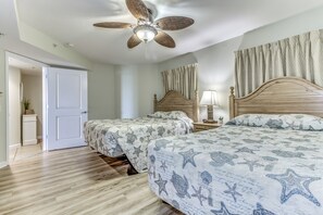 Un dormitorio con dos camas, un ventilador de techo y una puerta que da a otra habitación.