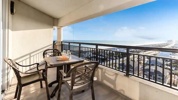 Ein Balkon mit Tisch und Stühlen, der Blick auf die Küste mit Gebäuden und Strand bietet.