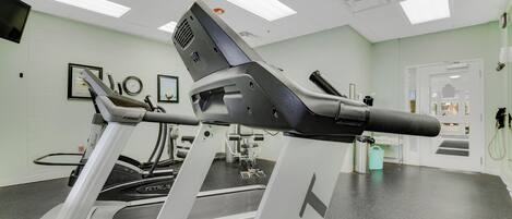 Un gimnasio con cintas de correr, equipo de ejercicio y una pared blanca con cuadros enmarcados.