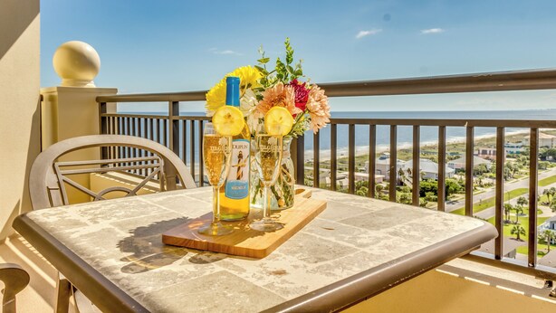 A balcony with a table set for two, featuring a floral arrangement and two bottles of Magnolier wine.