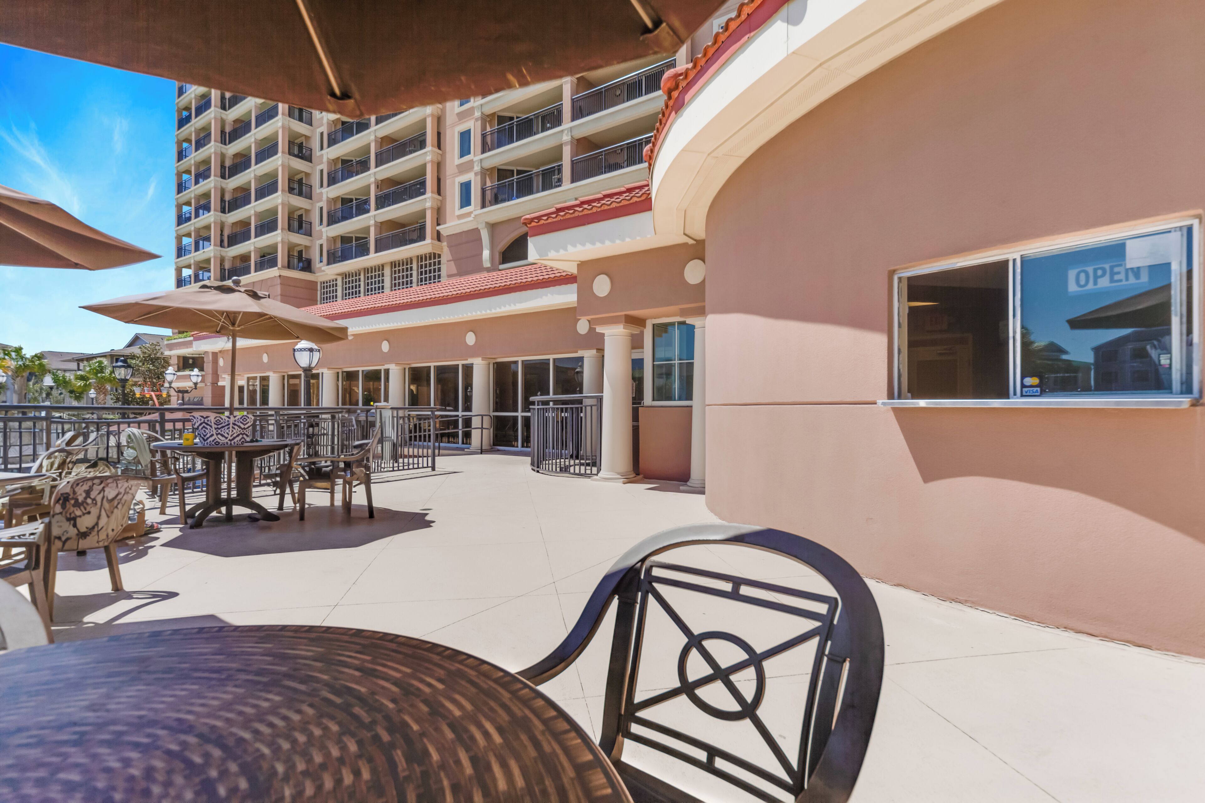 An outdoor patio area with tables and chairs, a building with balconies, and a sign indicating an open establishment.