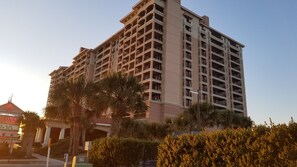 A multi-story hotel with balconies, surrounded by palm trees and a well-maintained hedge.
