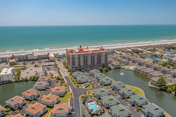A coastal residential area with a large hotel featuring multiple floors and a distinctive orange roof, surrounded by smaller houses and a body of water.