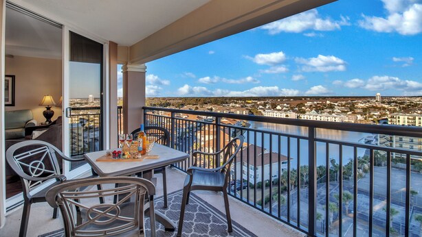 A balcony with a table and chairs, overlooking a cityscape and a body of water. - 3BR- 11th floor- North Lake & Oceanview Back Corner|Free Parking| Resort Access| (North Myrtle Beach)