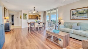 A spacious living room with a light green sofa, a wooden coffee table, and a dining area with a table and chairs. - 3BR- 11th floor- North Lake & Oceanview Back Corner|Free Parking| Resort Access| (North Myrtle Beach)