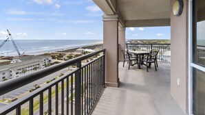 Een balkon met een tafel en stoelen, met uitzicht op een strand en een bouwplaats.