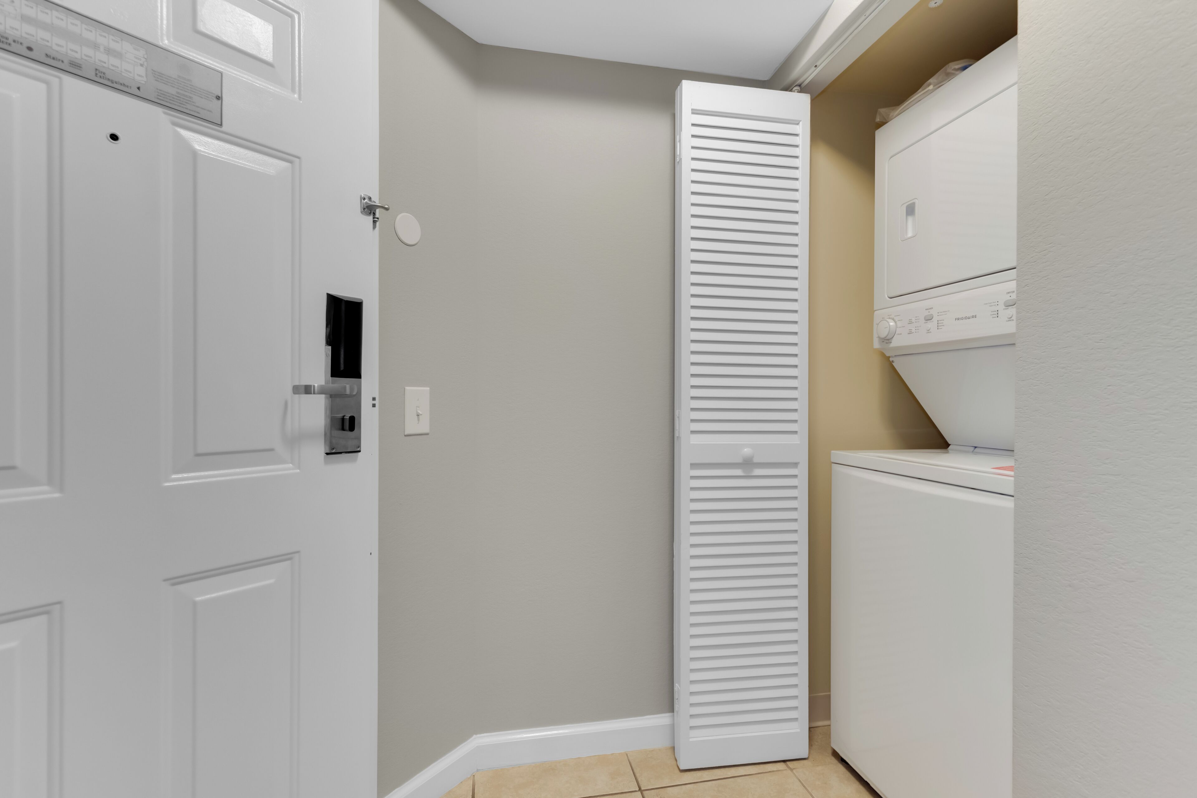Un cuarto de lavado con una puerta blanca, un electrodoméstico alto de color blanco y una pared color beige.