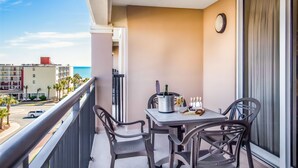 A balcony with a table and chairs, a clock on the wall, and a view of the ocean and buildings. - 3BR- 5th floor- North Lake & Oceanview Back Corner|Free Parking| Resort Access| (North Myrtle Beach)