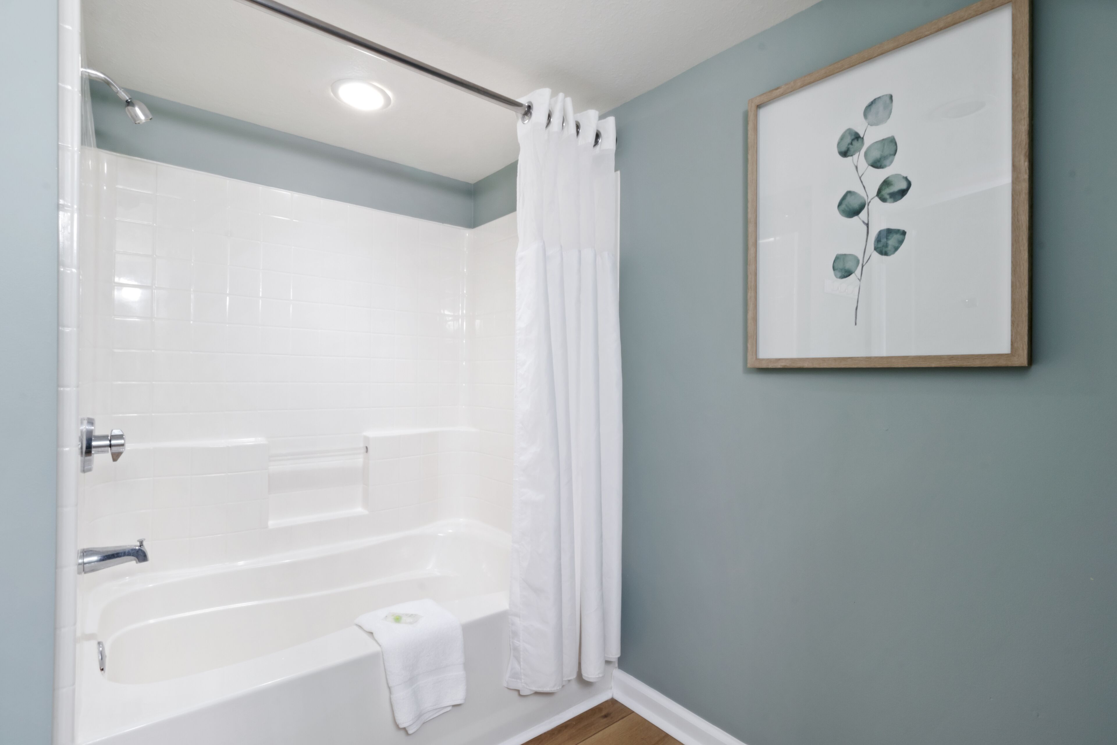A bathroom with a bathtub, a shower, and a framed artwork on the wall.