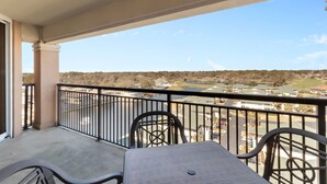 A balcony with a table and chairs, overlooking a residential area with houses and a green landscape.