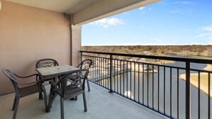 A balcony with a table and chairs, overlooking a body of water and distant landscape.