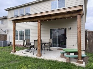 A covered patio with a table and chairs, a wooden pergola, and a green picnic table.