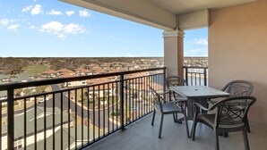 Ein Balkon mit Tisch und Stühlen, der auf ein Wohngebiet mit Häusern und einer Straße blickt.
