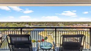 A balcony with two chairs and a small table, overlooking a residential area and a body of water.