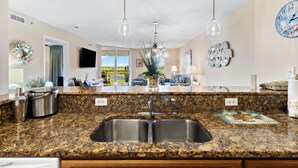 A kitchen with granite countertops, stainless steel sink, and overhead pendant lights.