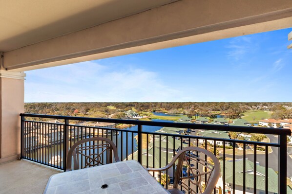 A balcony with a table and chairs, overlooking a golf course and a body of water.