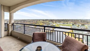A balcony with a glass table and two chairs, overlooking a river and residential area. - 3BR- 14th floor- Lake & Golf View condo|Short walk to beach| Resort Access| (North Myrtle Beach)