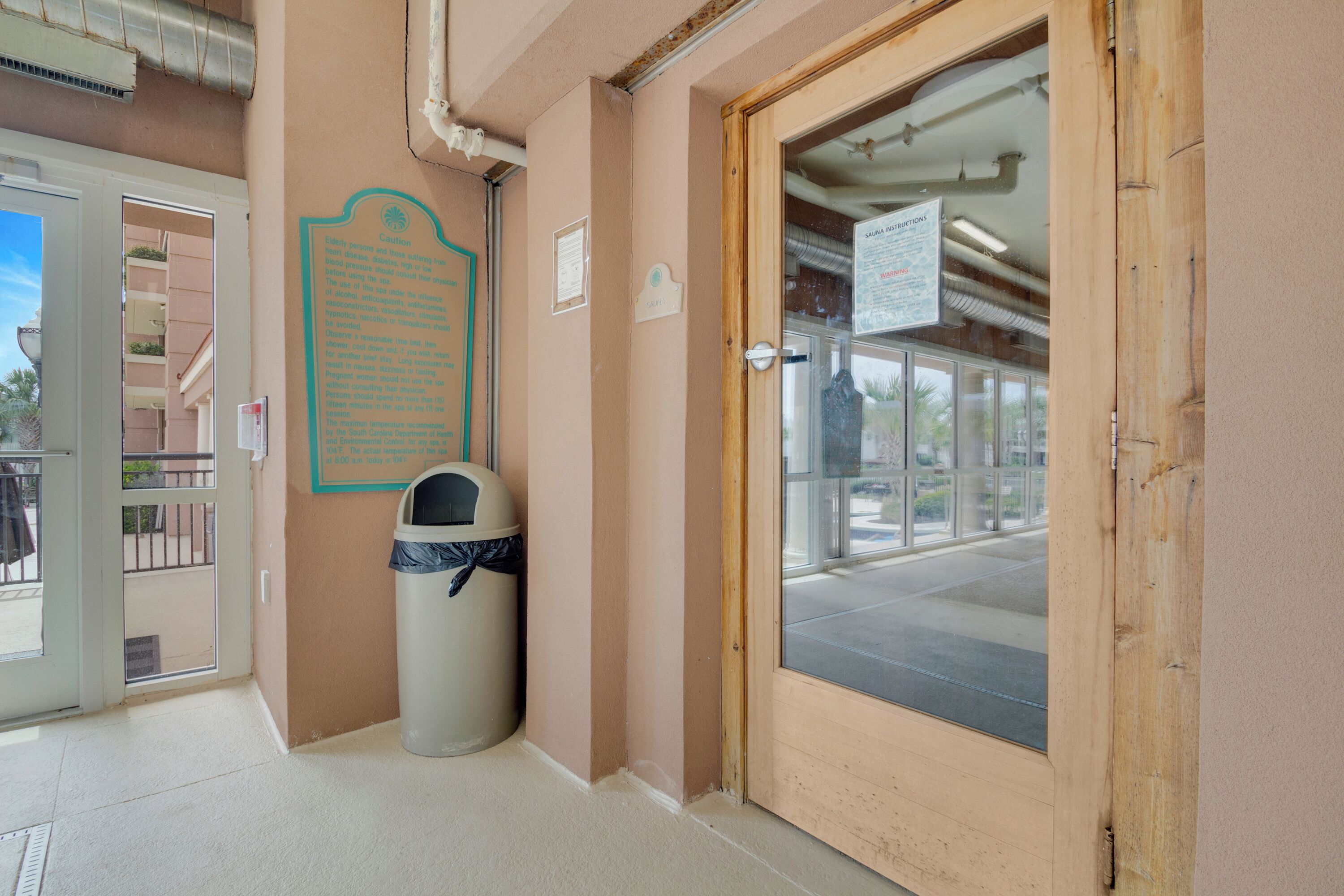A hotel entrance with a wooden door, a trash bin, and a sign with directions.