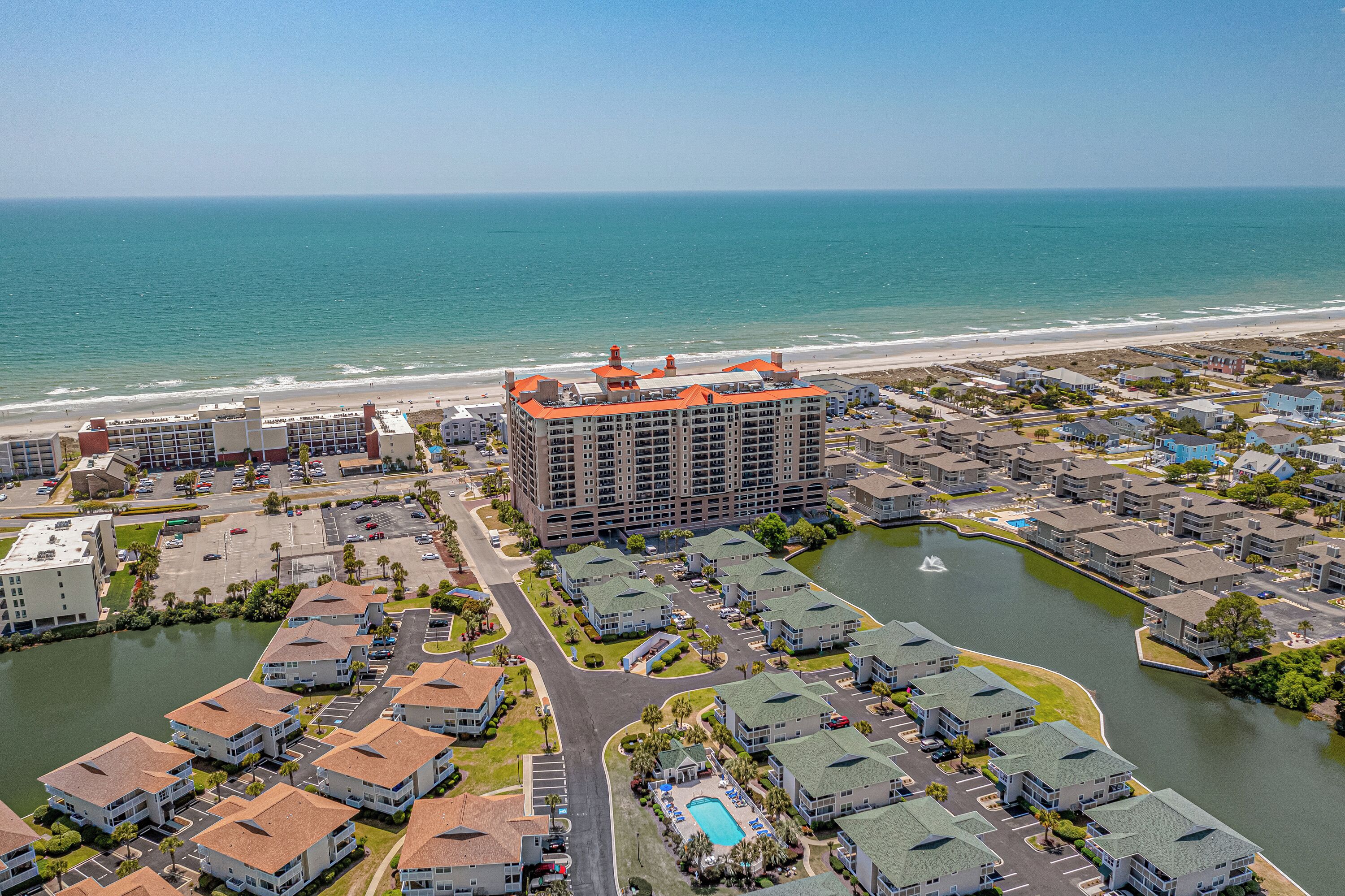 A coastal residential area with a large hotel featuring multiple floors and a distinctive orange roof, surrounded by smaller houses and a body of water.