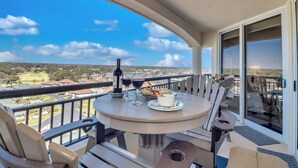 Un balcon avec une table dressée pour deux personnes, agrémentée d’une bouteille de vin, de verres et d’une assiette de nourriture.