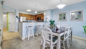 Una cocina moderna con armarios de madera, un refrigerador de acero inoxidable y una barra con taburetes blancos.