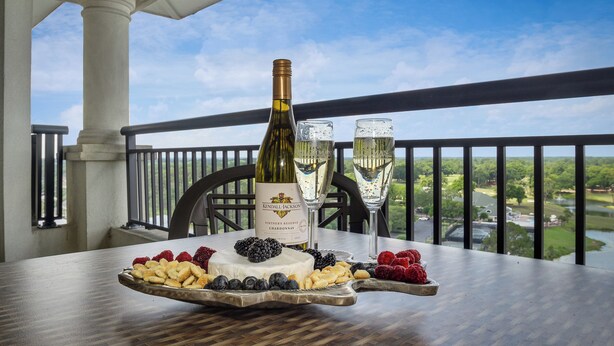 Una mesa con una botella de vino, copas y una bandeja de fruta en un balcón con vistas.