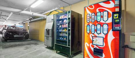 A parking garage with vending machines, including a Coca-Cola branded one, and a car in the background.