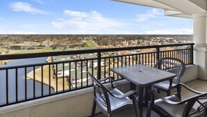A balcony with a table and chairs, overlooking a residential area and a body of water.