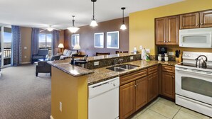 A modern kitchen with granite countertops, wooden cabinets, a white stove, and a dining area with a sofa and chairs.