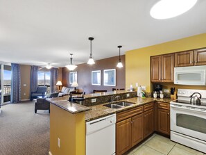 A modern kitchen with granite countertops, wooden cabinets, a white stove, and a dining area with a sofa and chairs. - 3BR- 15th floor- Lake & Golf View condo|Short walk to beach| Resort Access| (North Myrtle Beach)