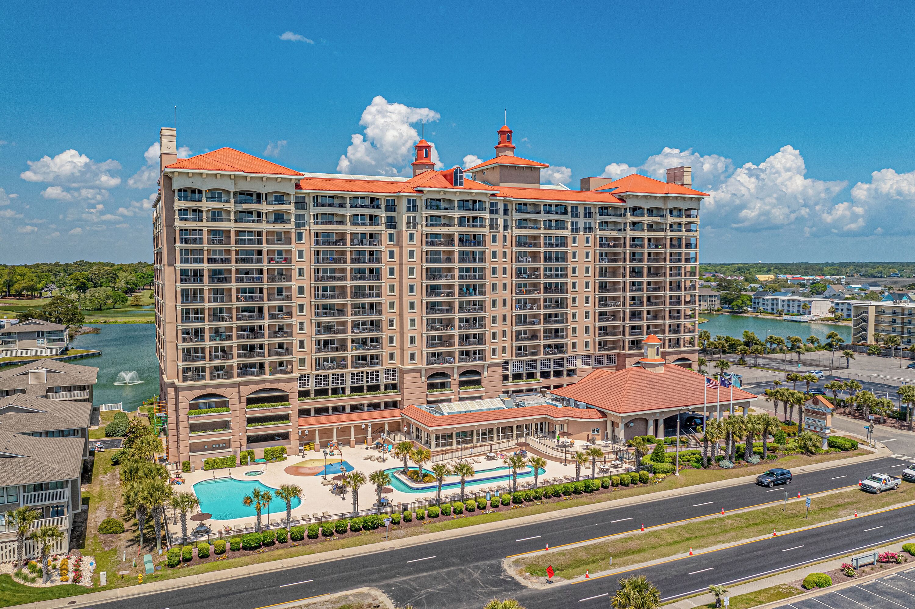 A large hotel with multiple floors, a swimming pool, and a view of a body of water.
