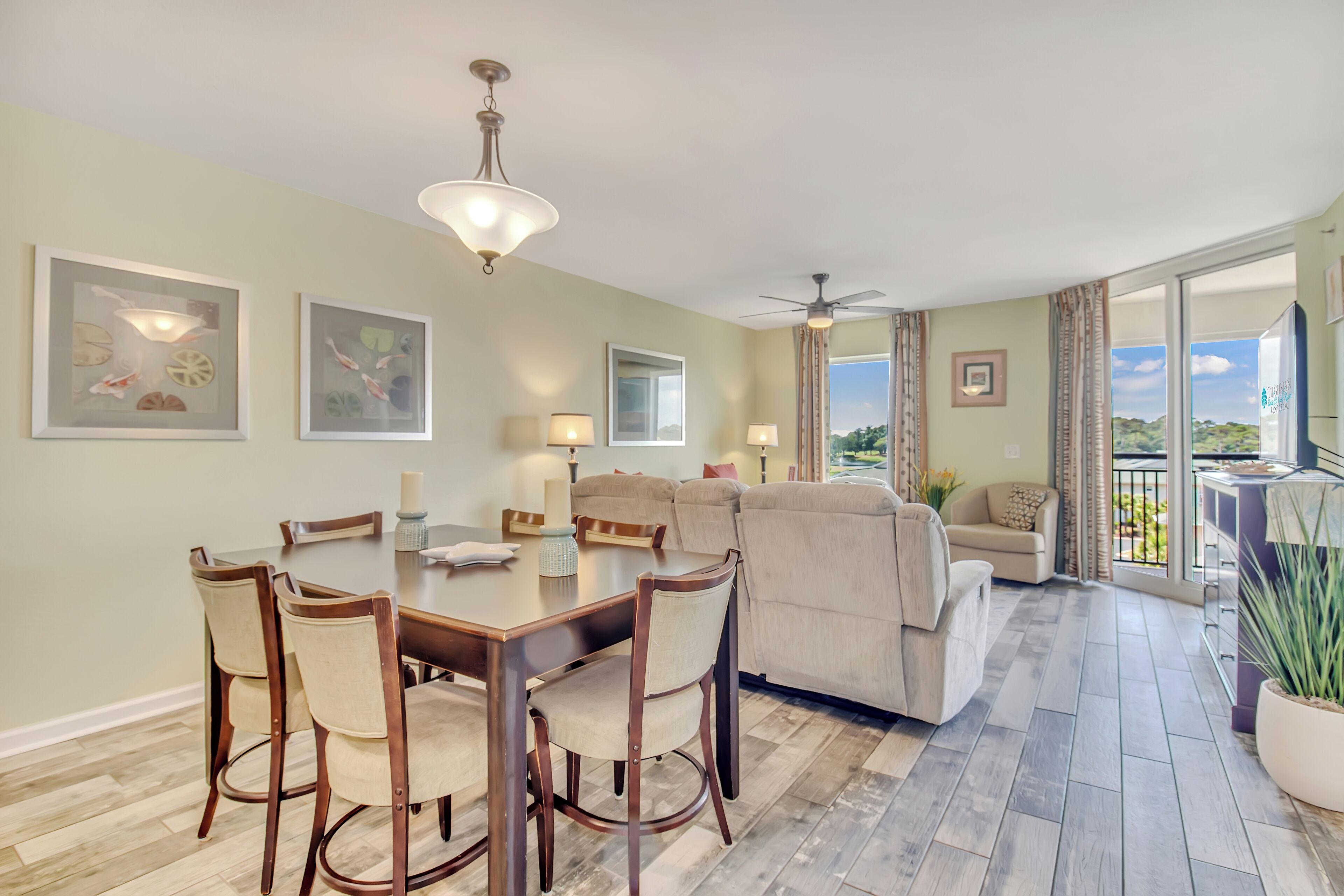 A spacious living area with a dining table, chairs, a sofa, and a balcony with a view.