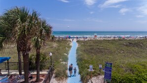 Ein Küstenpfad führt zum Meer, gesäumt von Palmen und Strandsonnenschirmen.