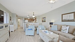 A spacious living room with a sofa, armchairs, and a coffee table. A kitchen is visible in the background with wooden cabinets and a dining area. - 3BR- 6th floor- Lake & Golf View condo|Short walk to beach| Resort Access| (North Myrtle Beach)