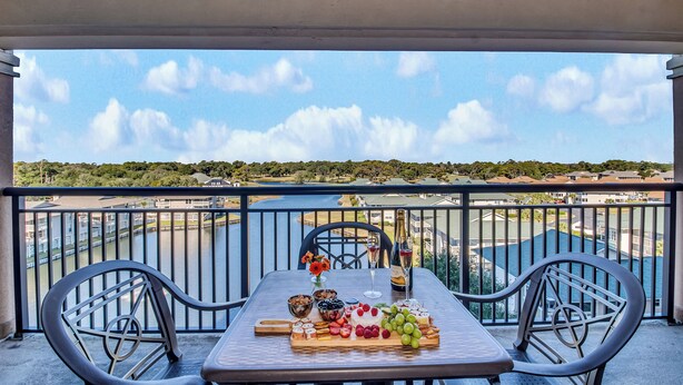 A balcony with a table set for a meal, overlooking a body of water and a distant landscape. - 3BR- 7th floor- Lake & Golf View condo|Short walk to beach| Resort Access| (North Myrtle Beach)