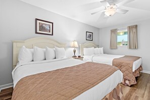 Habitación de hotel con dos camas, un ventilador de techo y una ventana con cortinas.