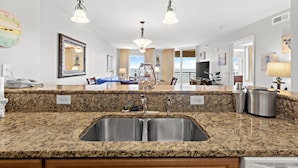 Cocina con encimeras de granito, lavamanos de acero inoxidable, iluminación colgante y vistas al comedor.