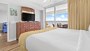 Habitación de hotel con una cama grande, televisión, cómoda de madera y balcón con vista al cielo.