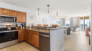Una cocina moderna con armarios de madera, microondas integrado y lavavajillas. Hay una isla grande con un fregadero y una zona de comedor con una silla y una mesa.