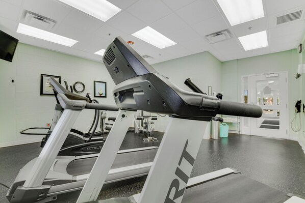 A gym with treadmills, exercise equipment, and a white wall with framed pictures.