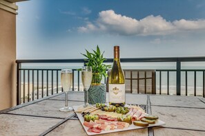 Een tafel met een wijnfles, glazen en een vleeswarenplank op een balkon met uitzicht op zee.